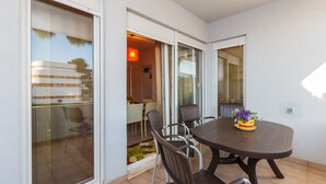 A dining area with a round table and chairs, a sliding glass door leading to an indoor space, and a small plant on the table. - Apartments Zenta (Split)