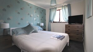 A bedroom with a bed, two bedside tables with lamps, a dresser, a television, and a window with curtains. - DO NOT USE (Doncaster)