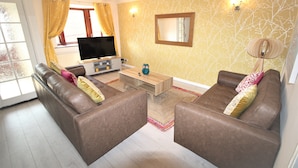 A living room with two brown leather sofas, a wooden coffee table, a flat-screen TV, and a patterned wall. - DO NOT USE (Doncaster)