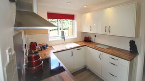 A modern kitchen with white cabinets, a wooden countertop, and a red kettle. - DO NOT USE (Doncaster)