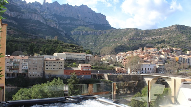 Une vue depuis un balcon donnant sur une ville, avec une montagne en arrière-plan, un pont et un jacuzzi.