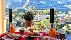 Une table de petit-déjeuner avec des croissants, des pizzas et du jus de fruits, le tout disposé devant un paysage de montagne.