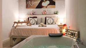 Une chambre avec une grande baignoire, un lit agrémenté de coussins décoratifs, un climatiseur fixé au mur et un panneau au-dessus du lit.