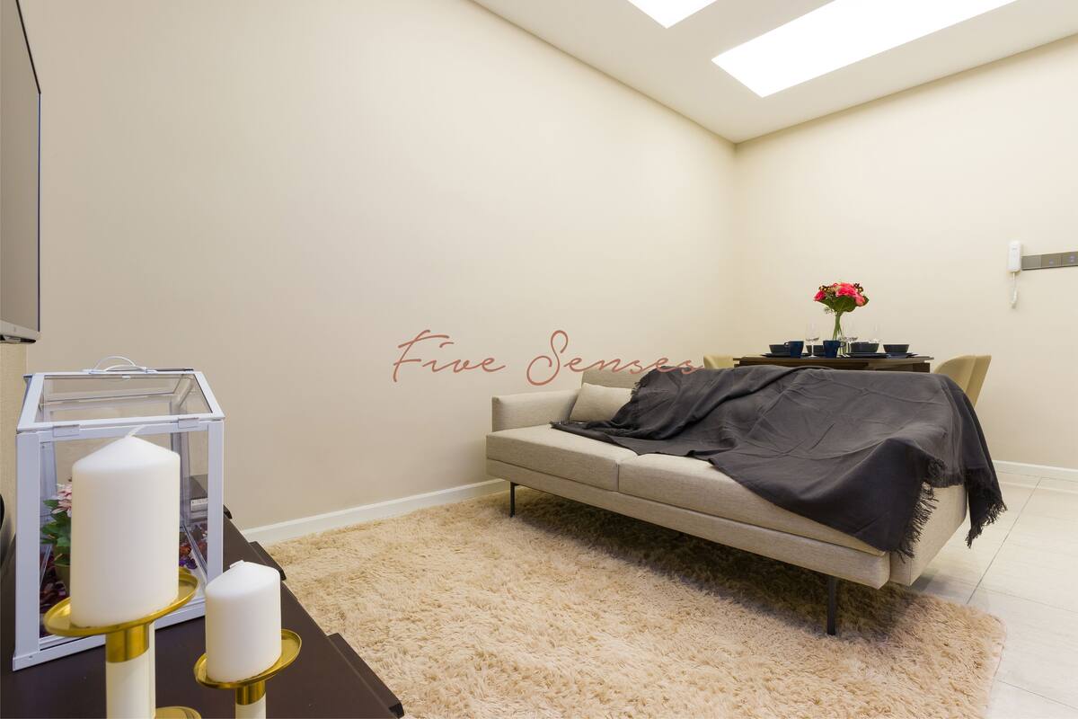 A modern living room with a sofa, a glass table with candles, and a wall-mounted phone.