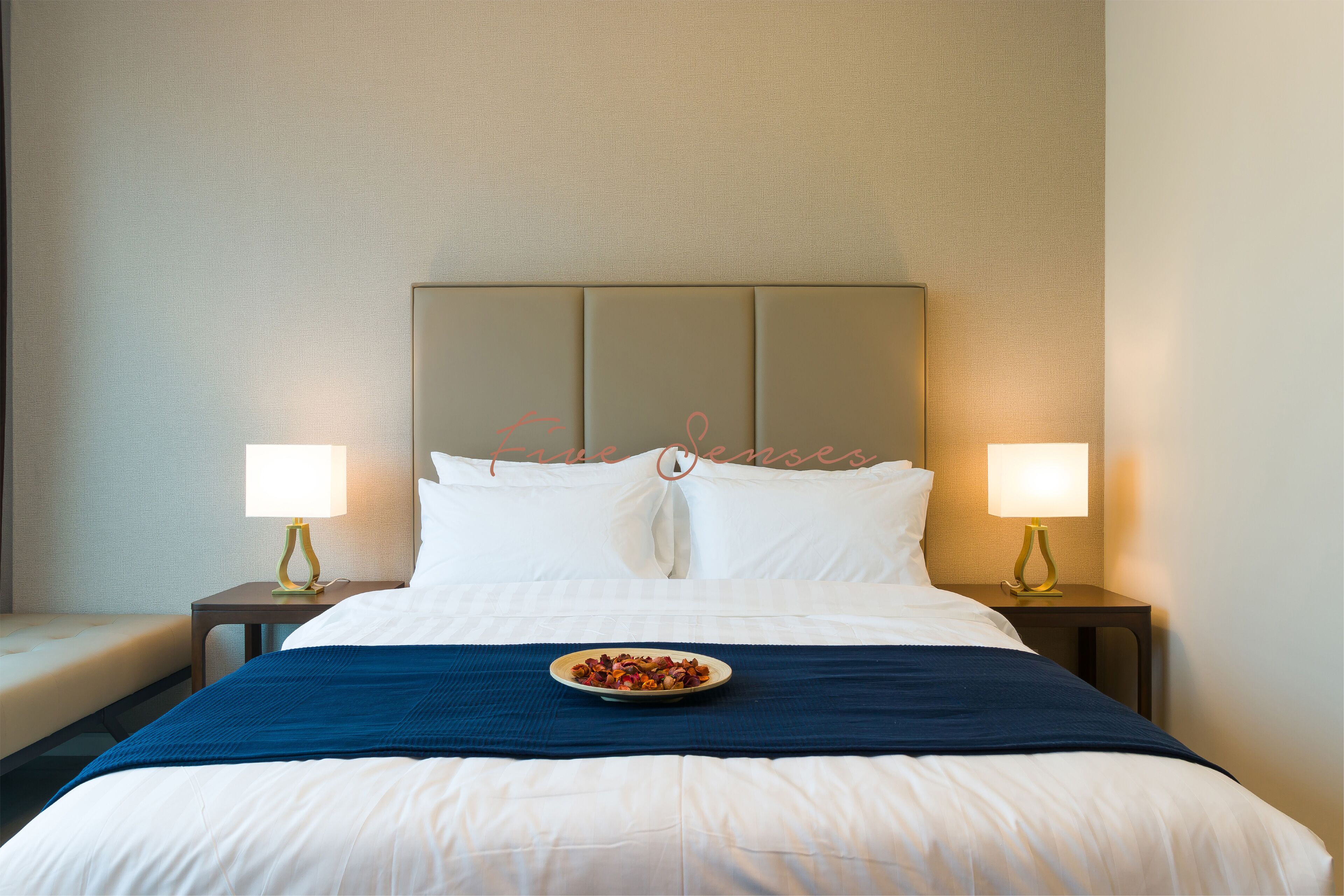 A hotel room with a large bed, two bedside tables with lamps, a blue bedspread, and a plate of food on the bed.