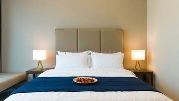 A hotel room with a large bed, two bedside tables with lamps, a blue bedspread, and a plate of food on the bed.