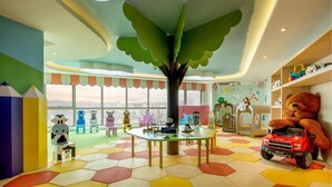 Un salón infantil vibrante con un techo con forma de árbol, suelo de hexágonos de colores y diversos juguetes y muebles.