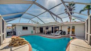 A covered swimming pool with lounge chairs and a stack of wooden planks. - 5 O'clock Somewhere - Private Elec. Heated Pool - WIFI - Streaming TV - BBQ (Cape Coral)