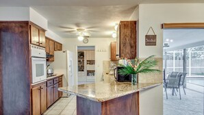 A kitchen with wooden cabinets, a central island, a clock, and a sign that reads "It's 5 o'clock somewhere." - 5 O'clock Somewhere - Private Elec. Heated Pool - WIFI - Streaming TV - BBQ (Cape Coral)