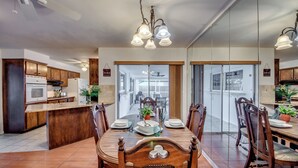 A modern kitchen with wooden cabinets, a central island, and a dining area with a large table and chairs. - 5 O'clock Somewhere - Private Elec. Heated Pool - WIFI - Streaming TV - BBQ (Cape Coral)
