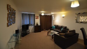 A living room with a glass coffee table, a dark sofa, a television, and a decorative wall piece. - Zen Apartments  Canary Wharf (London)