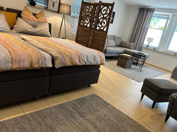 Een moderne slaapkamer met een groot bed, een slaapbank, een klein tafeltje en een decoratieve scheidingswand.