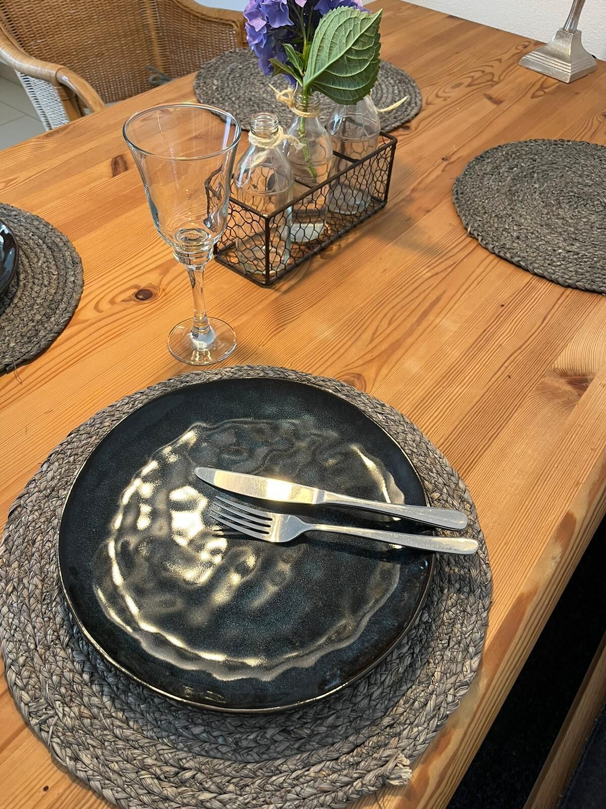 Ett matbord med en svart tallrik, silverbestick och ett genomskinligt glas.