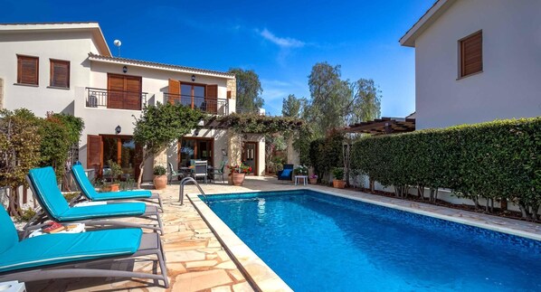 A pool area with lounge chairs, a stone deck, and a building with a balcony.