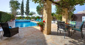 Un patio de piedra con piscina, mobiliario de exterior y una pérgola.