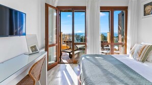 A bedroom with a bed, a desk, a chair, and a view of the sea through large glass doors.
