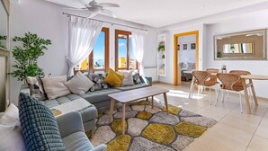 A modern living room with a sofa, coffee table, and dining area with wicker chairs.