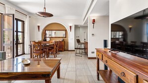 A spacious dining area with wooden furniture, a large wooden table, and a modern kitchen with a large flat-screen TV. - Apartment APD02 - Artemis (Kouklia)