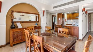 A spacious dining area with a wooden table and chairs, a large mirror, and a kitchen in the background. - Apartment APD02 - Artemis (Kouklia)