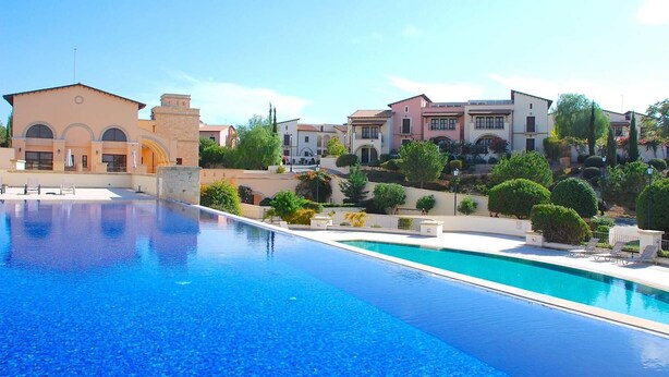A swimming pool with lounge chairs, surrounded by buildings with Mediterranean architecture. - Apartment APD02 - Artemis (Kouklia)