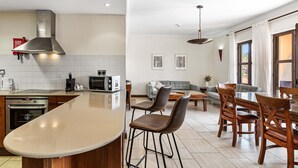 A modern kitchen with a large island, a dining area with wooden chairs, and a living room with a sofa and a coffee table. - Apartment APD02 - Artemis (Kouklia)
