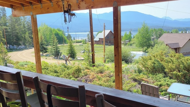 Eine Holzterrasse mit Stühlen und Tisch mit Blick auf eine malerische Landschaft, Berge und einen See.