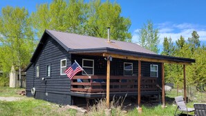 Eine Blockhütte mit einer amerikanischen Flagge, einer Veranda und einem Holzstapel.