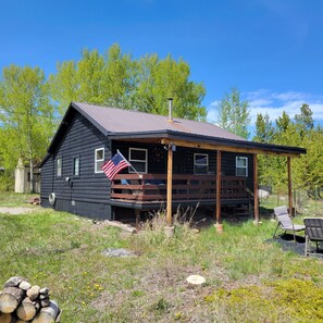 A log cabin with an American flag, a porch, and a stack of firewood. - Quaint Cabin Viewing Shadow Mountain Lake, Mountain Views and Lake Access nearby (Grand Lake)