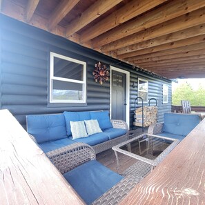 A covered outdoor seating area with a blue sofa, wicker chairs, and a glass table. - Quaint Cabin Viewing Shadow Mountain Lake, Mountain Views and Lake Access nearby (Grand Lake)