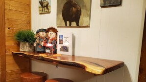 Eine rustikale Holztheke mit drei Hockern, einem Willkommensschild und Wildtiergemälden an der Wand.