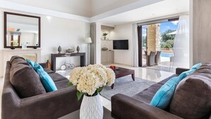 Un salón moderno con un conjunto de sofá, una mesa de centro con flores, un televisor y vistas a un patio exterior con piscina.