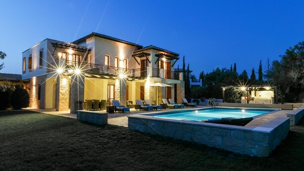 Una casa de dos pisos con piscina, mobiliario exterior y un patio bien iluminado.