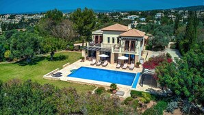 Una casa grande con piscina, rodeada de exuberante vegetación y vistas al mar.