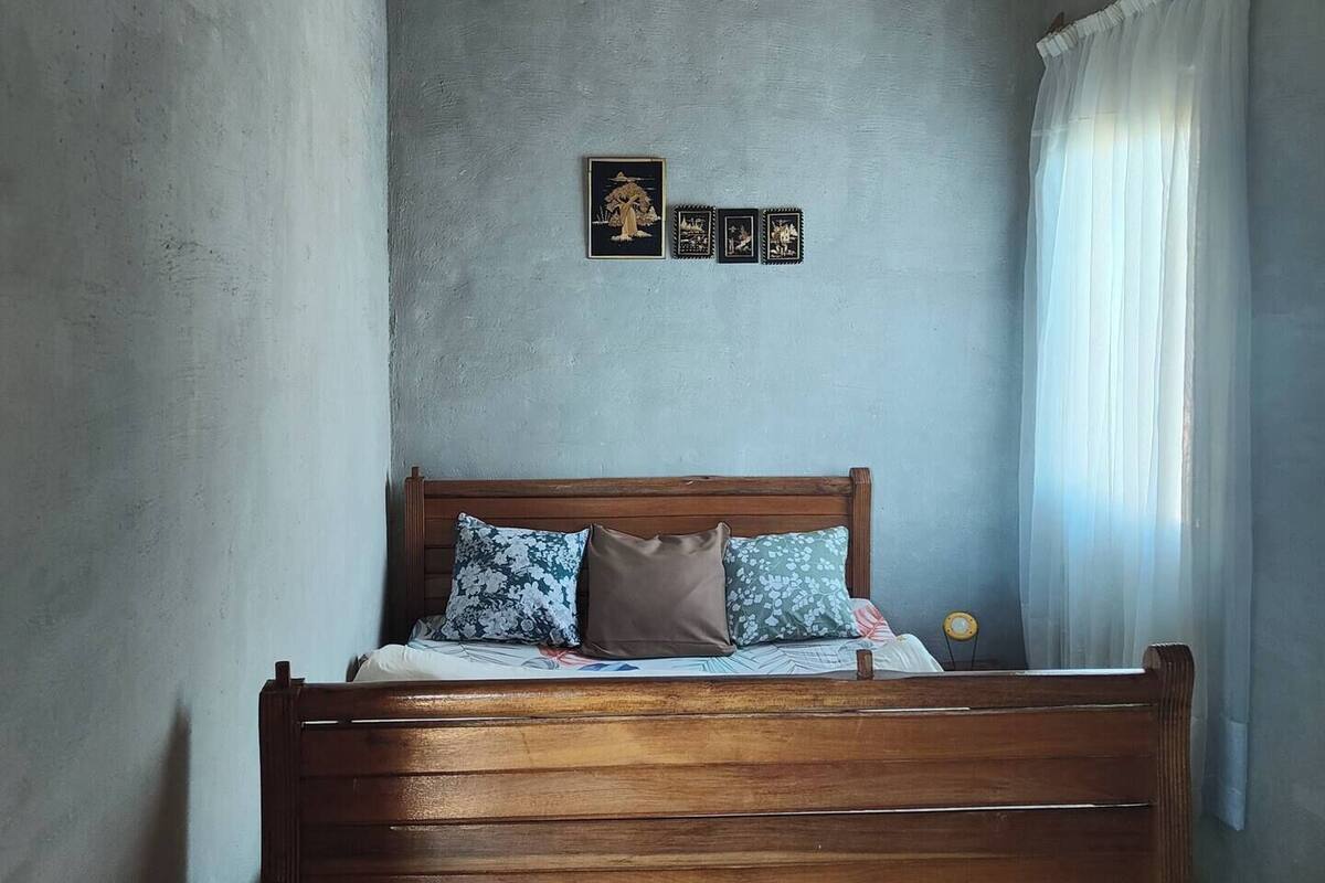 A bedroom with a wooden bed, a gray wall, and a ceiling with wooden panels.