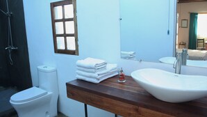 Een badkamer met een wit toilet, een wastafel met spiegel, en een raam met houten kader.