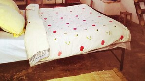 Een rustieke slaapkamer met een houten bed, een tafeltje, een stoel, een raam met gordijnen en een houten trap.