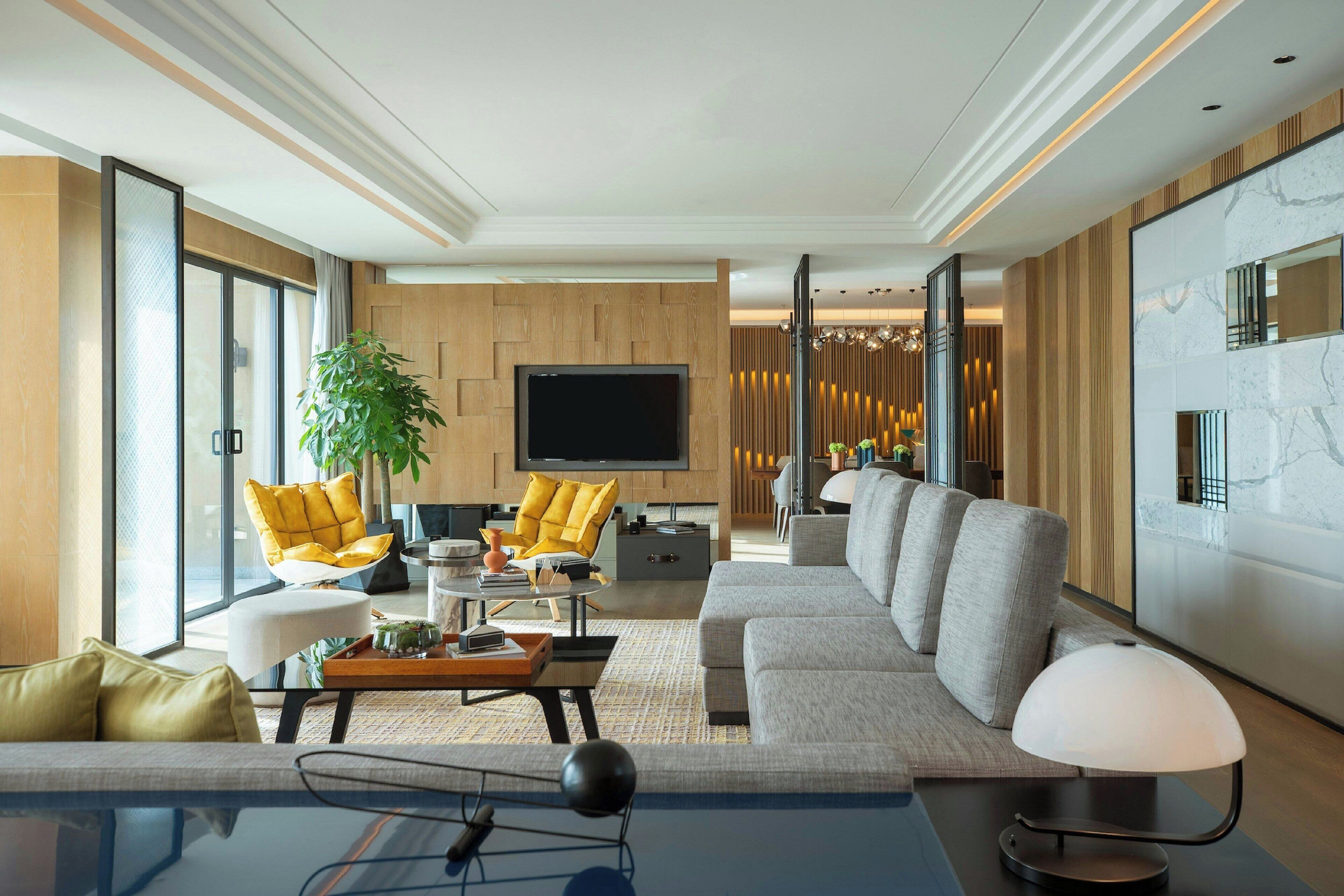 A modern living room with a large sofa, a coffee table, and a TV. There is a plant and a lamp on the table.