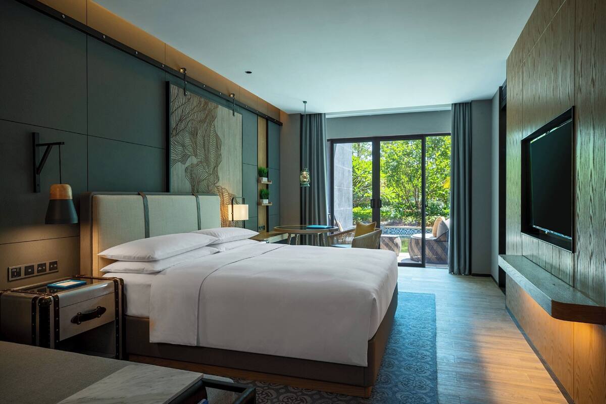A modern hotel room with a large bed, a desk, a TV, and a view of the outdoors.