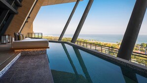 A modern infinity pool with a view of the ocean, a seating area with a sofa and cushions, and a large window overlooking the beach. - Renaissance Xiamen Hotel (Xiamen)