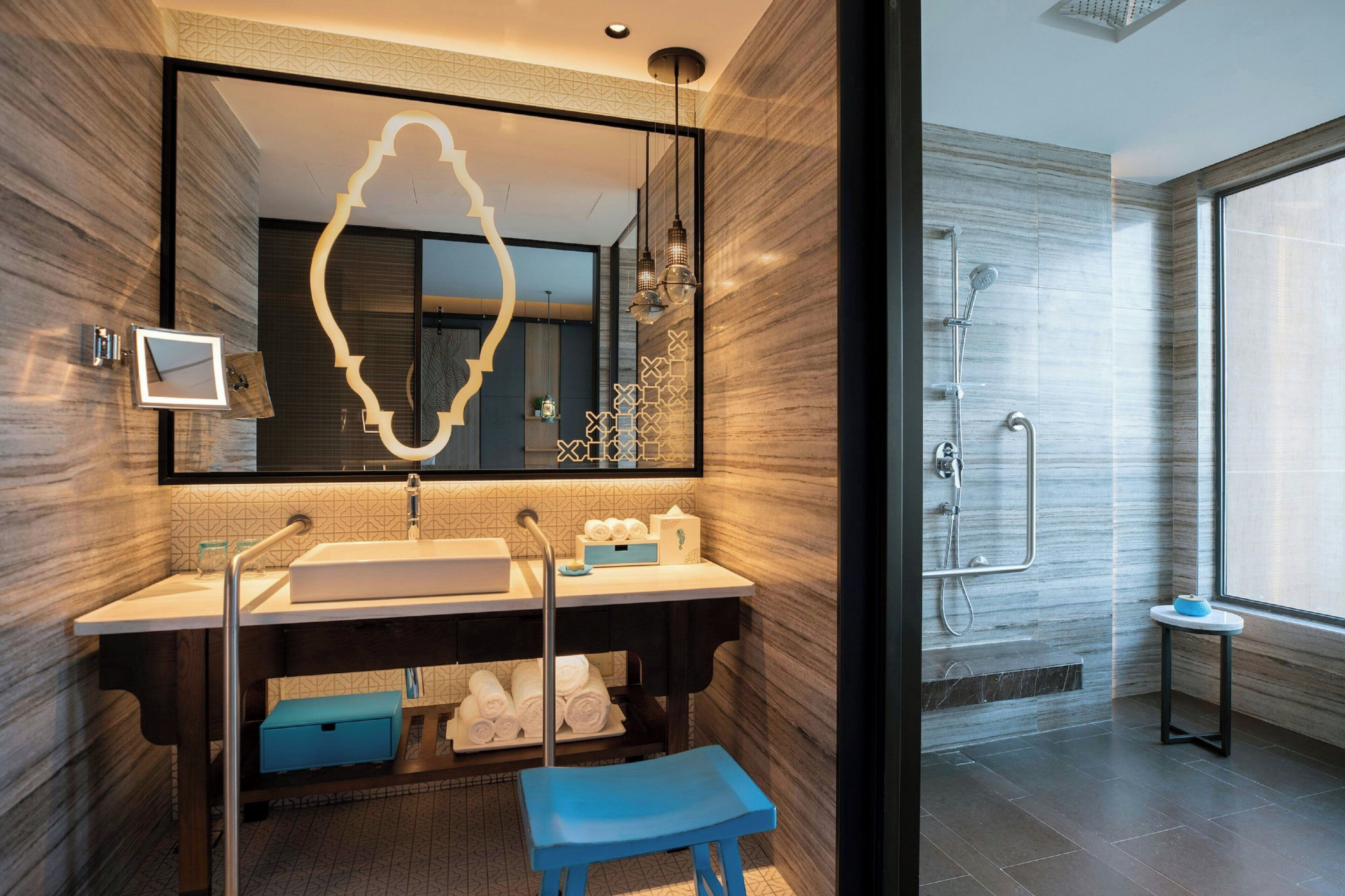 Ein modernes Badezimmer mit einem großen Spiegel, zwei Waschbecken, einer Dusche und einer blauen Bank.