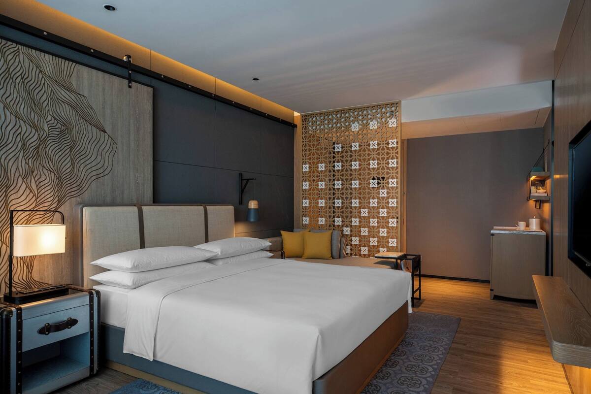 A modern hotel room with a large bed, bedside tables, a TV, and a decorative wall panel.