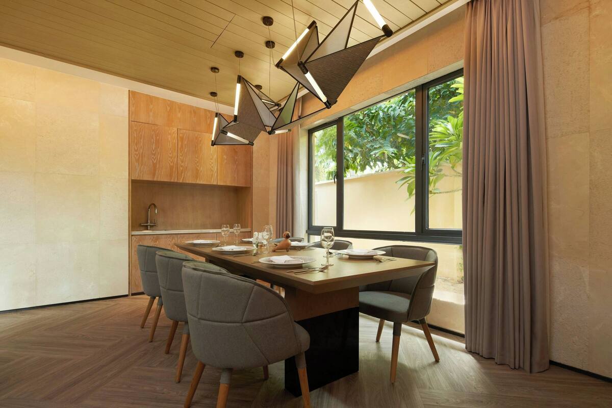 A modern dining area with a wooden table set for six, surrounded by grey chairs.
