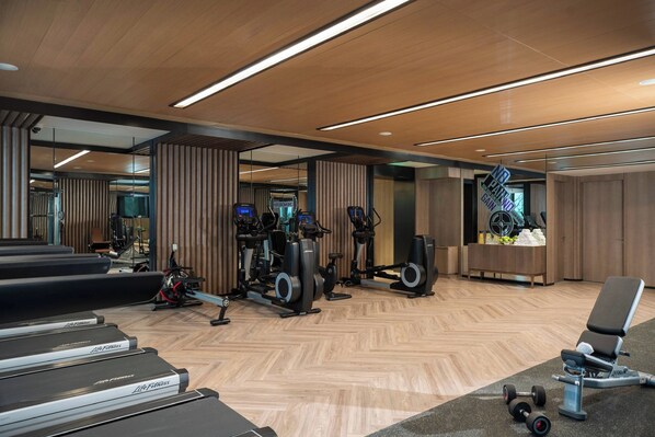 Une salle de sport moderne équipée de tapis de course, de vélos elliptiques et de matériel de musculation.