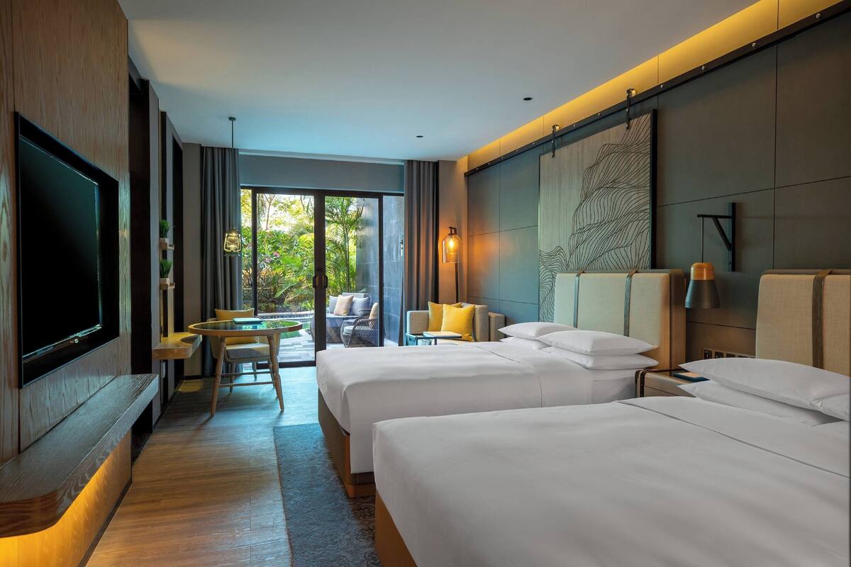 A hotel room with two beds, a flat-screen TV, a dining area with a table and chairs, and a view of the outdoors.