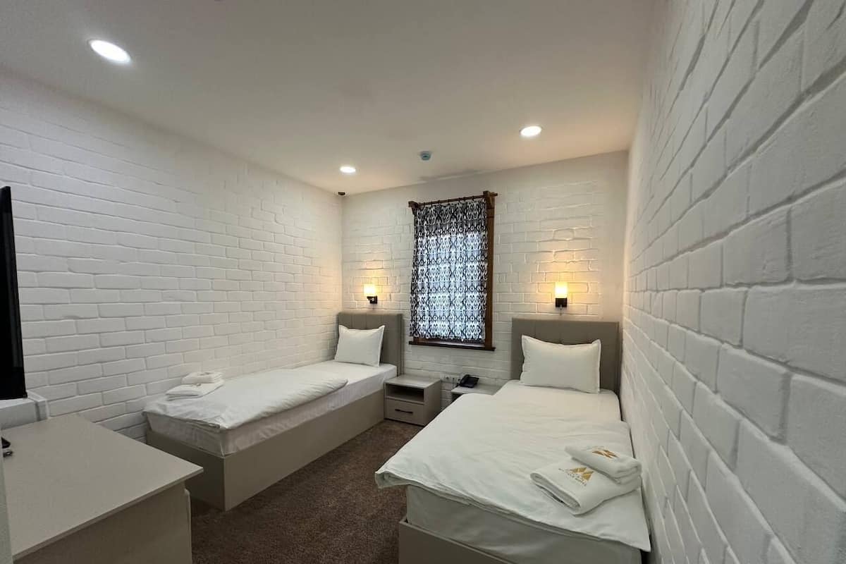 A room with two beds, a desk, and a window with patterned curtains.
