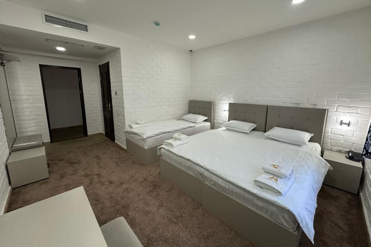 A modern hotel room with three beds, a small desk, and a bathroom.