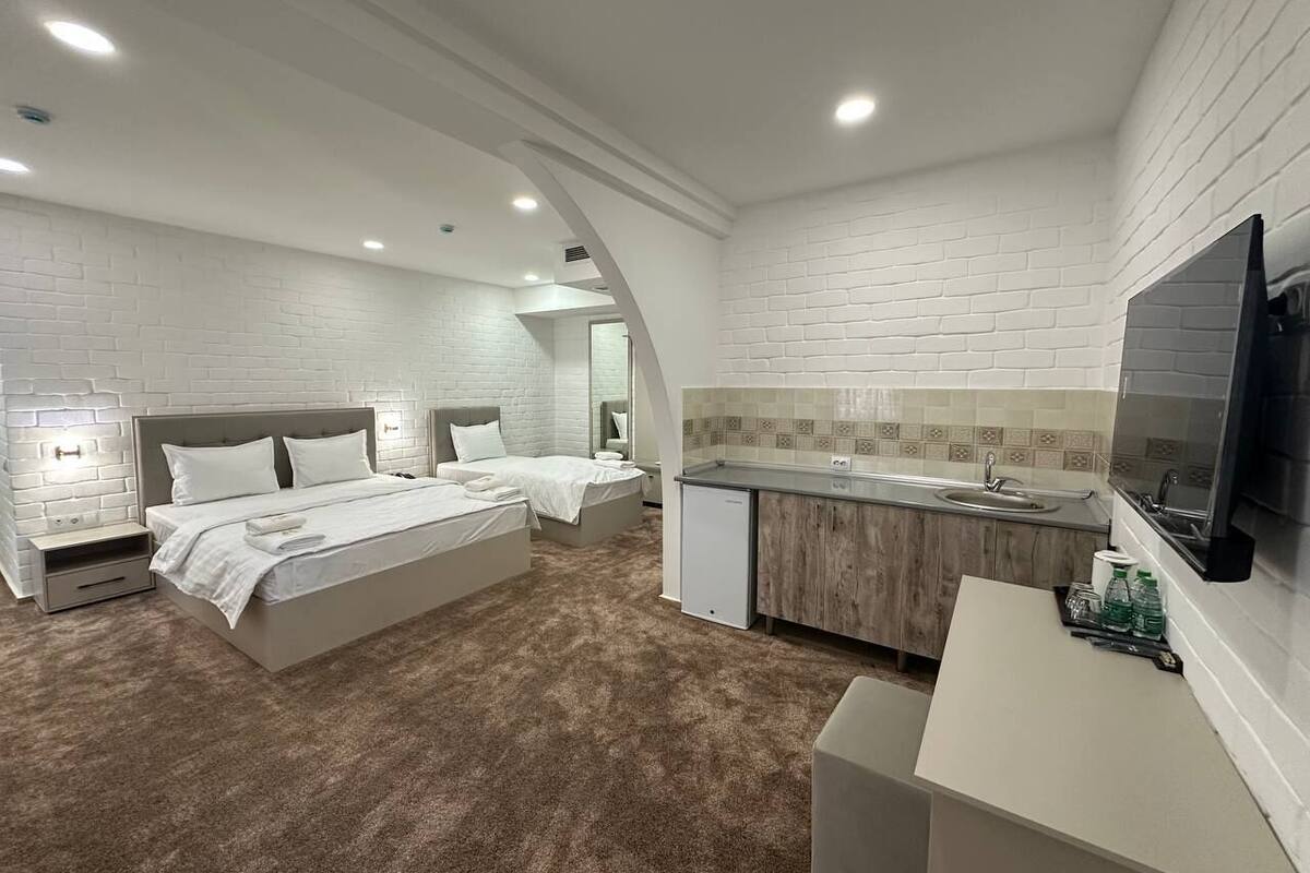 A modern hotel room with a large bed, a small kitchenette, and a TV.