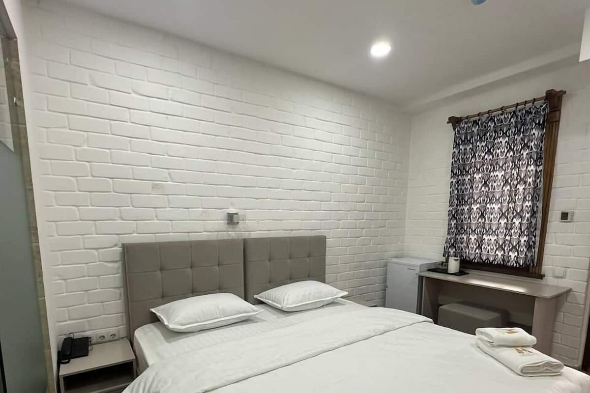 A hotel room with a large bed, a nightstand, a vanity with a mirror, and a window with a patterned curtain.