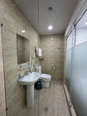 Un bany modern amb plat de dutxa de vidre, un lavabo amb mirall i un vàter.