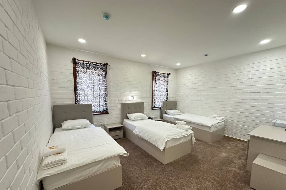 A hotel room with three single beds, a small desk, and a chair.